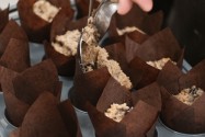 Muffin batter being spooned into brown tulip paper liners in a baking tray