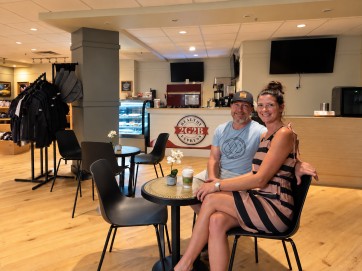 A couple sitting with coffee at a café table in front of the 2G2B Healthy Express counter